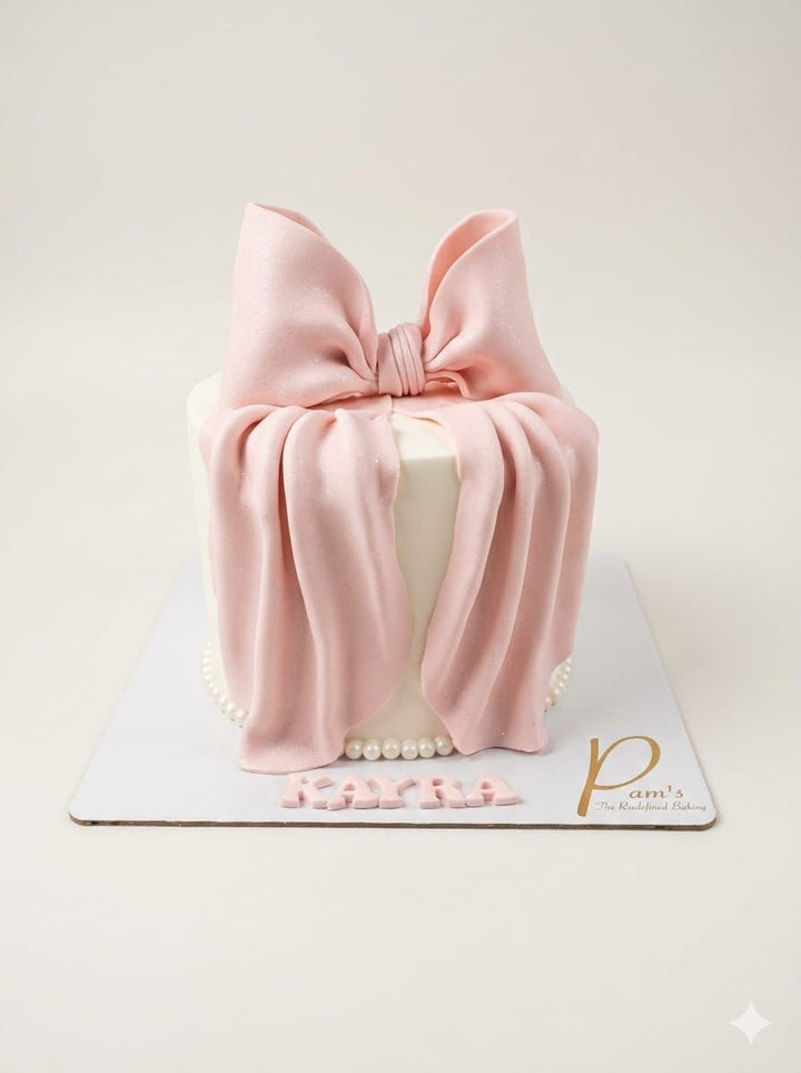 Cylindrical cake with a large pink bow on top, set against a light background.